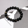 A stretch bracelet made of smooth, polished black obsidian and gold-flecked beads on a dark gray surface.