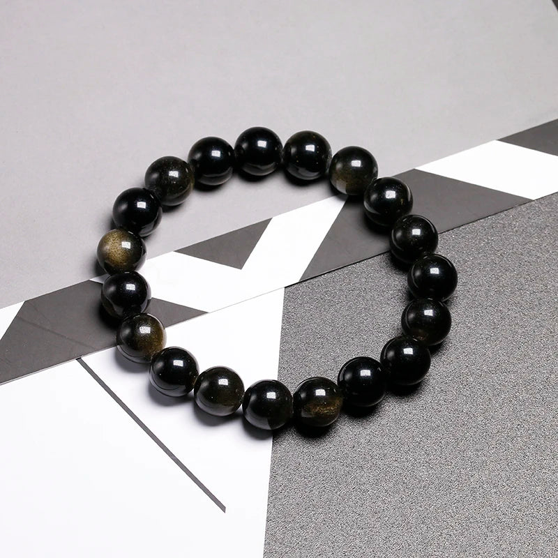 A stretch bracelet made of smooth, polished black obsidian and gold-flecked beads on a dark gray surface.