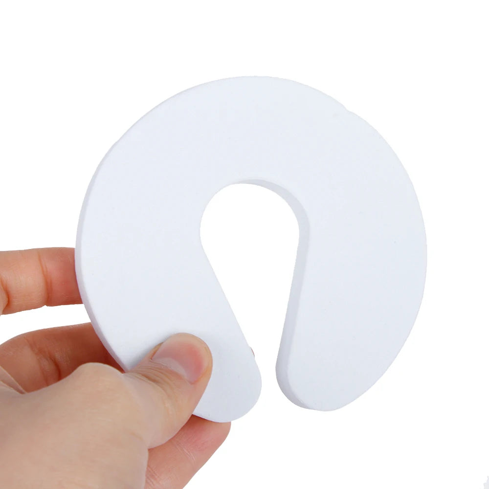 A white foam door stopper with a finger pinch protection design being held by a hand.