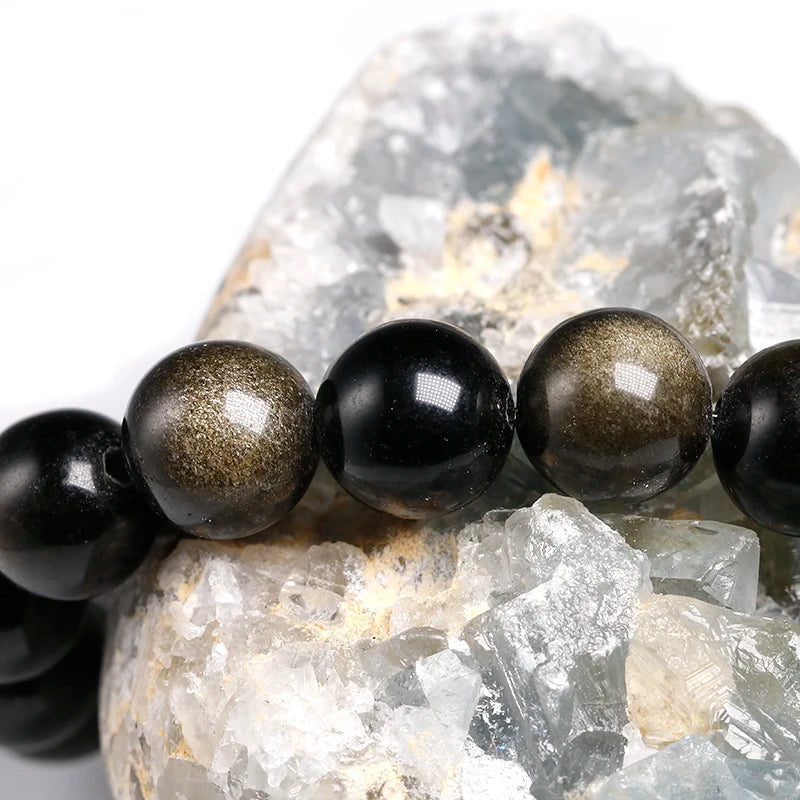 A stretch bracelet featuring polished black and gold obsidian beads set on a rough, translucent stone matrix.