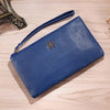 A dark blue Litchi-Grain PU leather long wallet with a strap and a gold logo resting on a wooden surface.