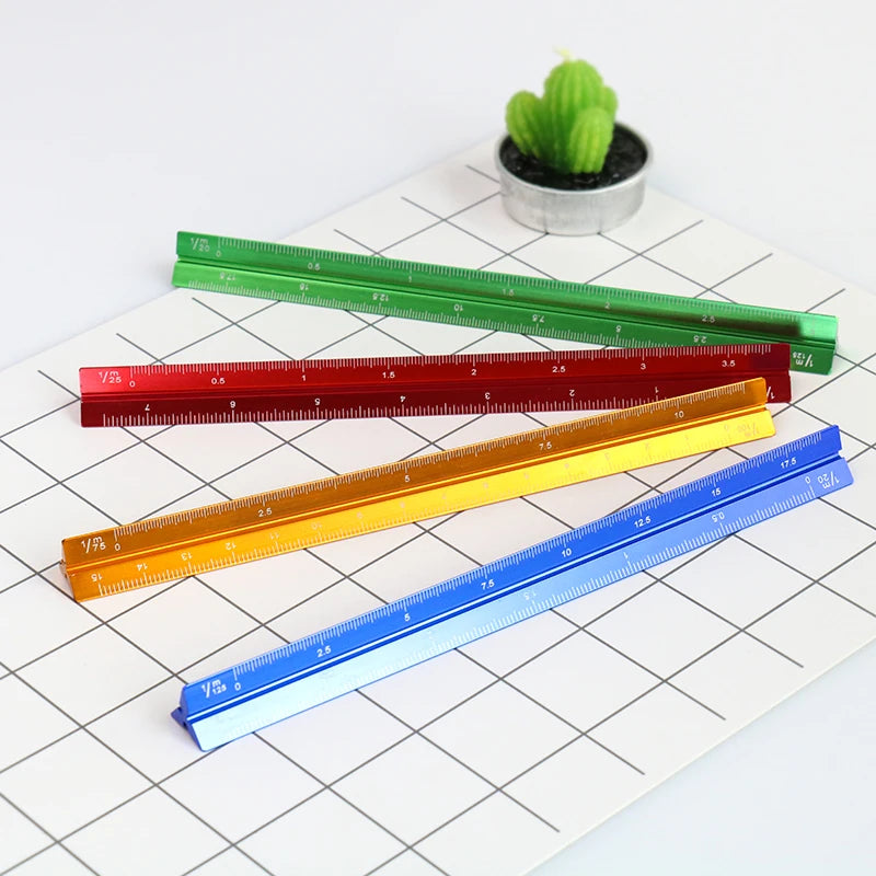 A collection of colorful aluminium triangular scale rulers laid on a white grid paper next to a small green cactus.