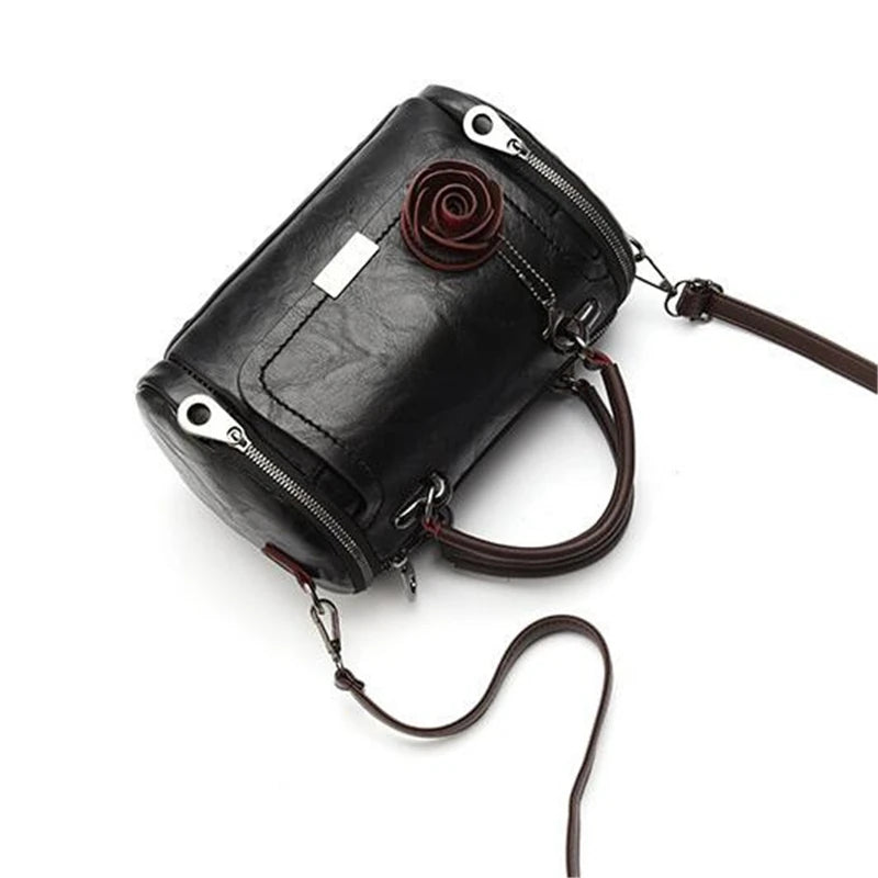 A black leather crossbody shoulder bag with a rose pendant and leather strap.