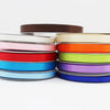 A stack of double-faced satin ribbon rolls in various colors, including brown, white, orange, green, pink, red, blue, and pur