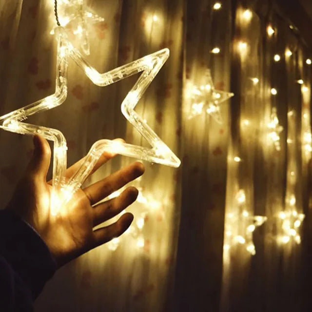 A hand holds a glowing, star-shaped light sculpture against a background of warm string lights.