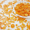 A pile of assorted wooden buttons in shades of orange and yellow scattered on a white surface.