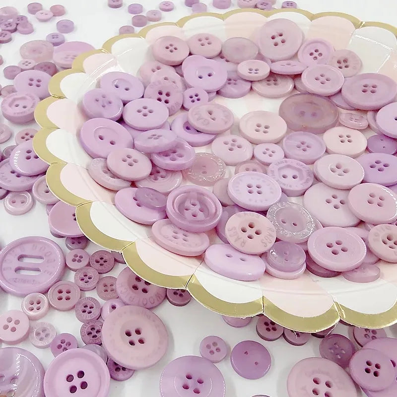 A variety of pink and purple wooden buttons are scattered across a white surface.