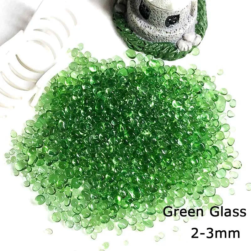 A pile of green glass pebbles measuring 2-3mm next to a small decorative stone figure.