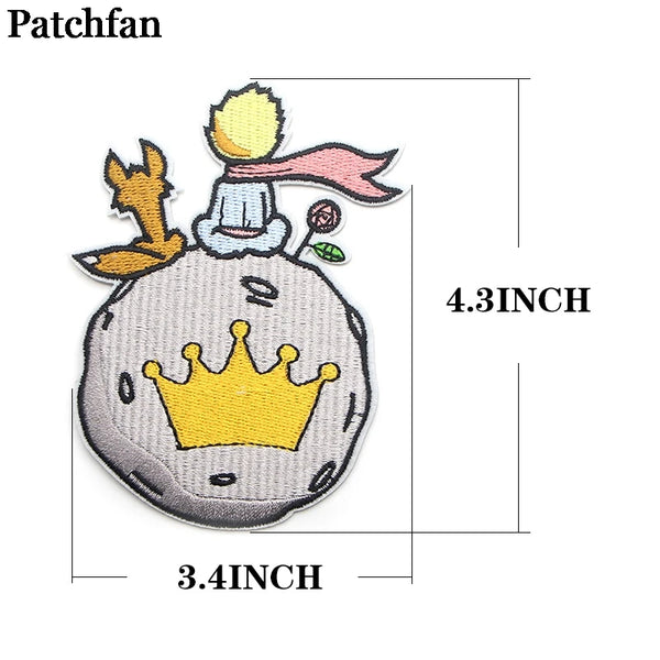 Eine gelbe Krone und eine Figur mit rosa Haaren sind auf einem grauen Patch gestickt.