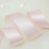 Light pink satin ribbon rolls laid out on a white surface.