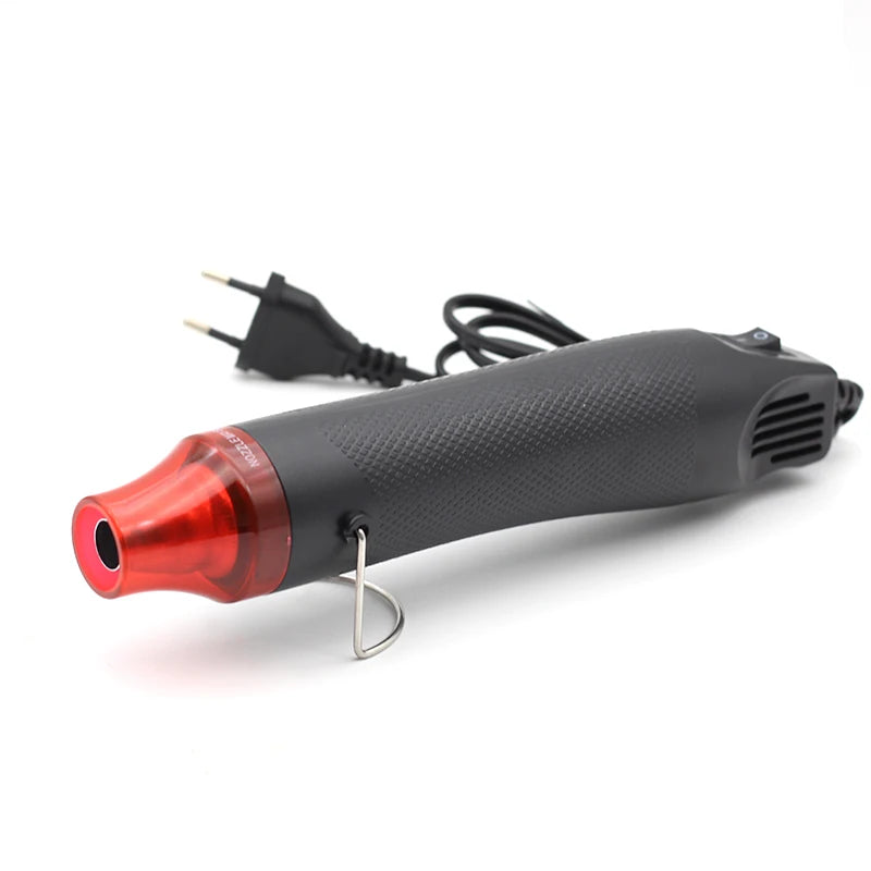 A black electric heat gun with a red tip and a metal hook is shown against a white background.