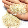 A hand holds a pile of light beige decorative stone pebbles measuring 2-3mm.