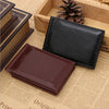 A black leather wallet is shown resting on a piece of parchment paper next to a wooden box and a pinecone.