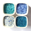 Four small white bowls filled with decorative blue and teal colored stone pebbles