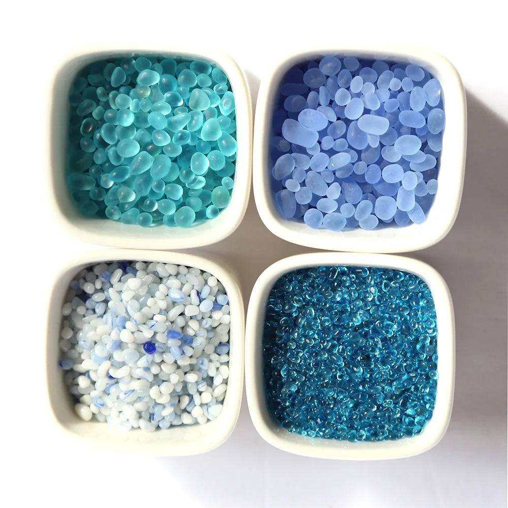 Four small white bowls filled with decorative blue and teal colored stone pebbles
