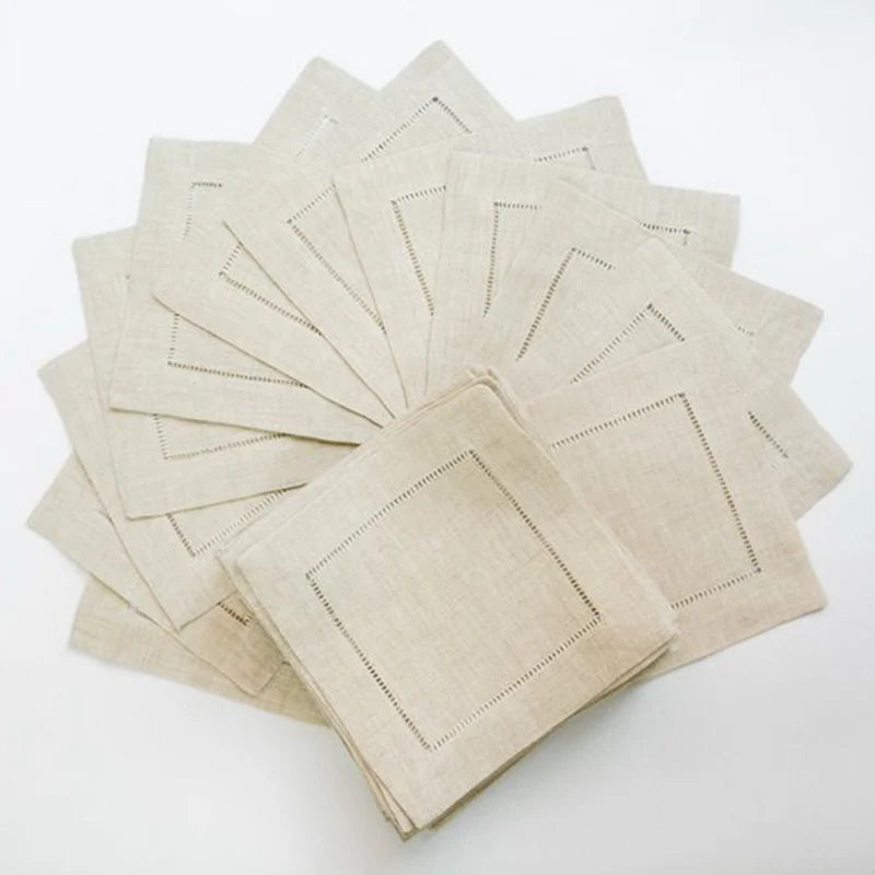 A stack of six natural linen hemstitch napkins folded and arranged on a white surface.