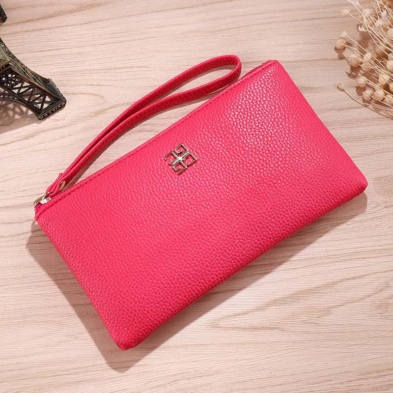 A bright pink Litchi-Grain PU leather long wallet with a strap and a phone pocket resting on a wooden surface.