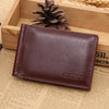 A brown leather wallet with a magnetic closure resting in a wooden box next to a pinecone.