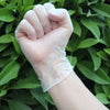 A hand wearing a disposable clear PVC glove is shown against a background of green leaves.