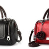 A black leather handbag with a floral pendant and a red leather version of the same bag.