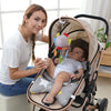 A woman holds a soft plush baby rattle toy with hanging bell and mobile on a stroller for newborns.