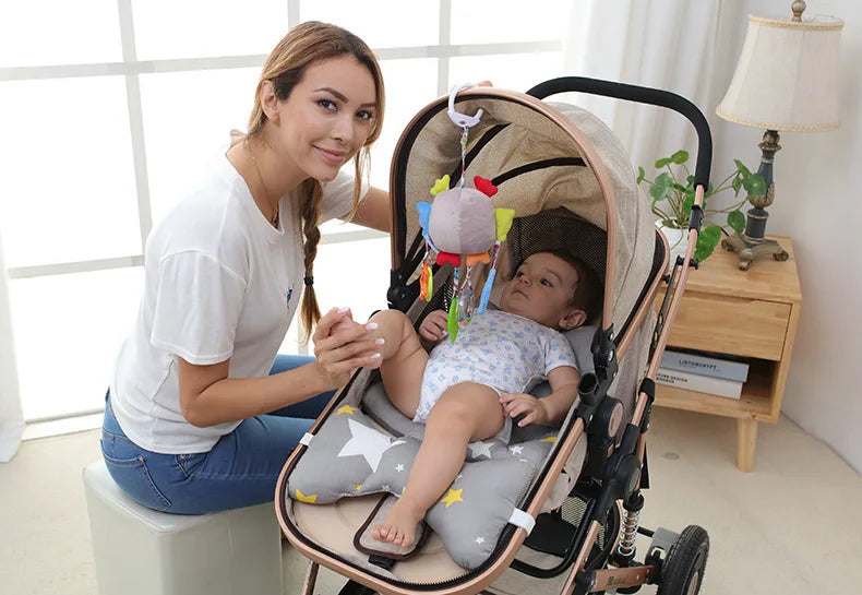 A woman holds a soft plush baby rattle toy with hanging bell and mobile on a stroller for newborns.