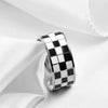A chunky silver ring with a black and white checkerboard enamel design worn on a white fabric.