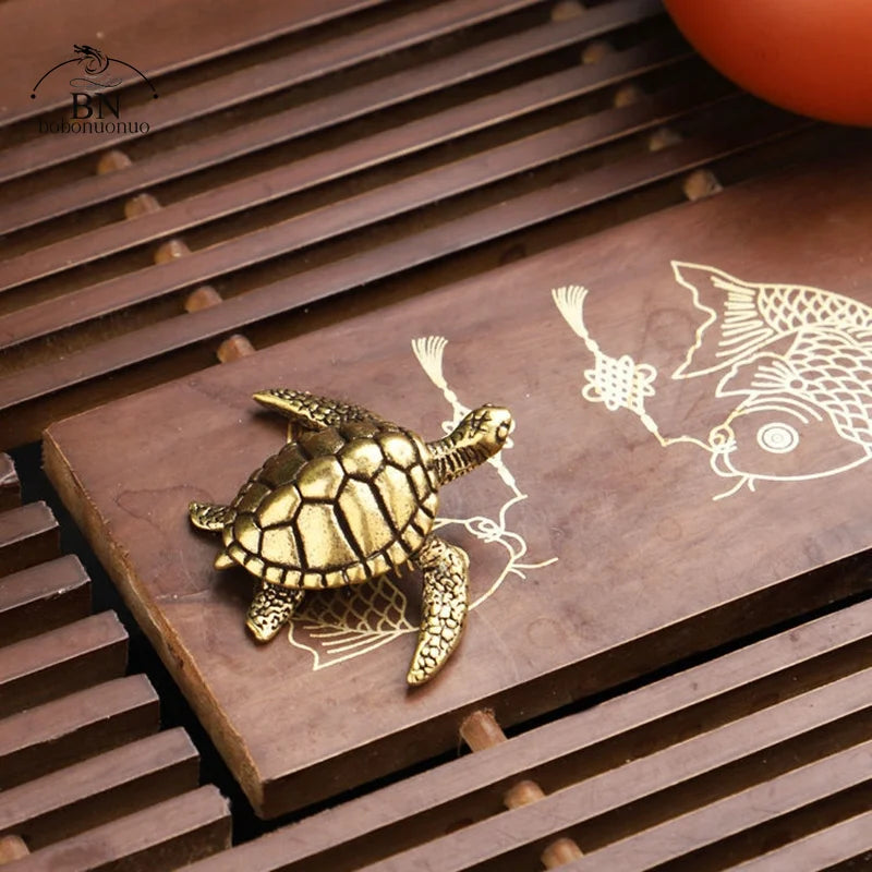 A golden copper turtle figurine is displayed on a wooden slab with an etched fish design, set against a dark brown background