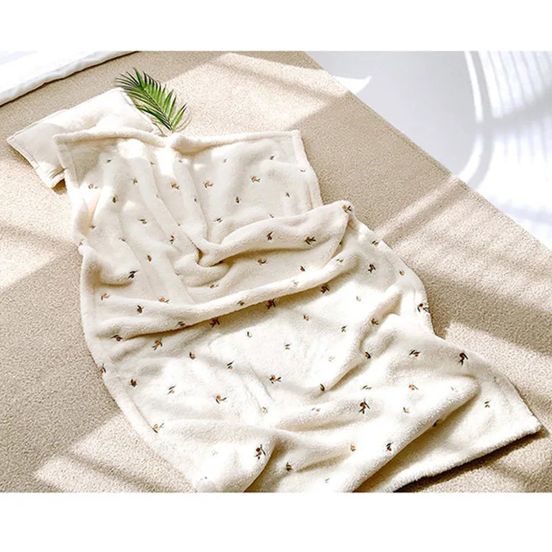 A cream-colored coral fleece baby blanket with subtle bear embroidery is draped on a light beige surface.