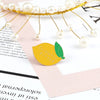 A gold wire fruit brooch pin with pearl-like beads is displayed on a pink paper background.