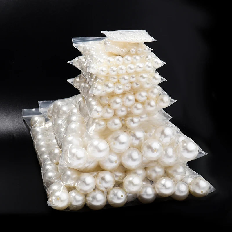 A pile of round white ABS imitation pearl beads for jewelry making displayed on a dark background.