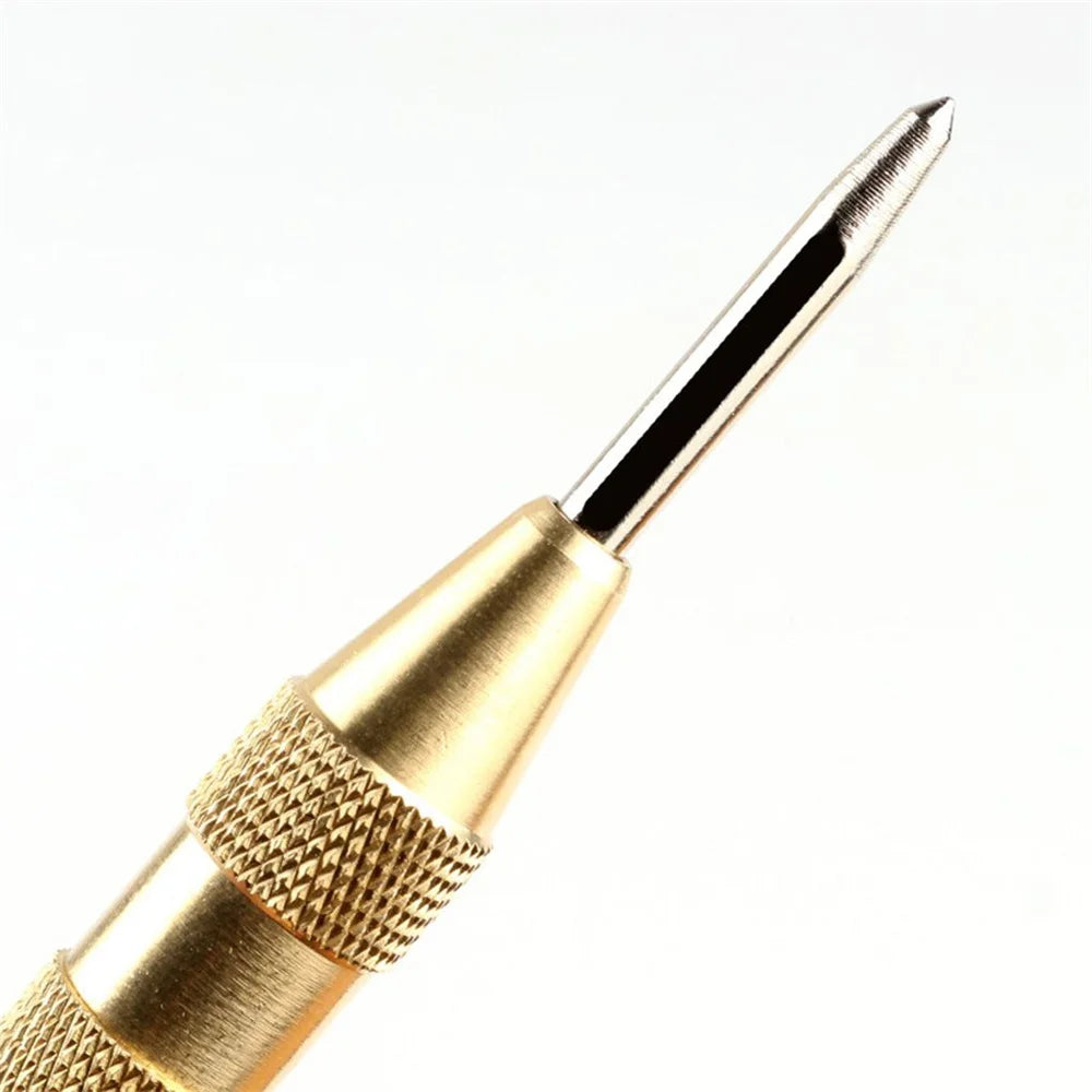 A close-up view of a gold-colored spring-loaded automatic center punch tool with a sharp point.