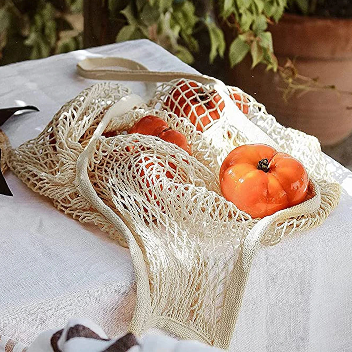 Two beige organic cotton mesh produce bags filled with small orange gourds resting on a white cloth.