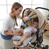 A woman is holding a baby in a soft plush stroller mobile featuring a cartoon animal rattle and hanging bell.