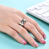 A hand wearing a chunky gold ring with a black and white checkerboard enamel design next to a white computer keyboard.