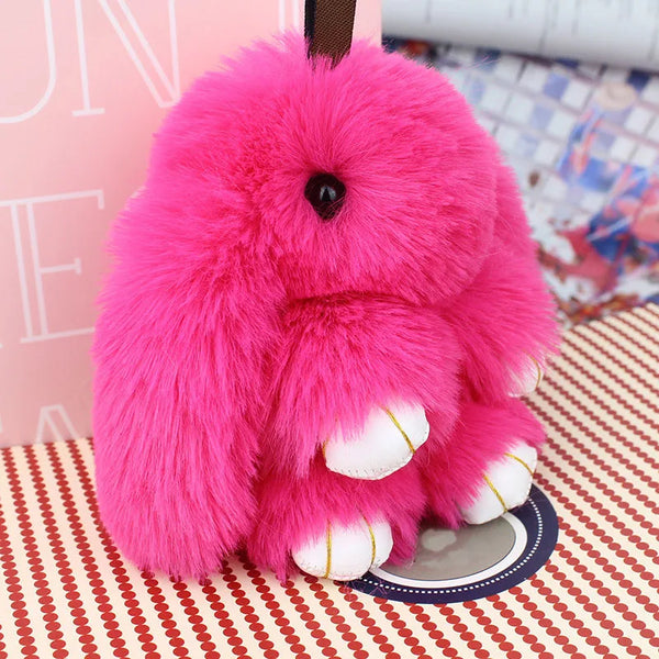 Un conejito peluche rosa brillante y esponjoso como llavero sobre una superficie estampada.