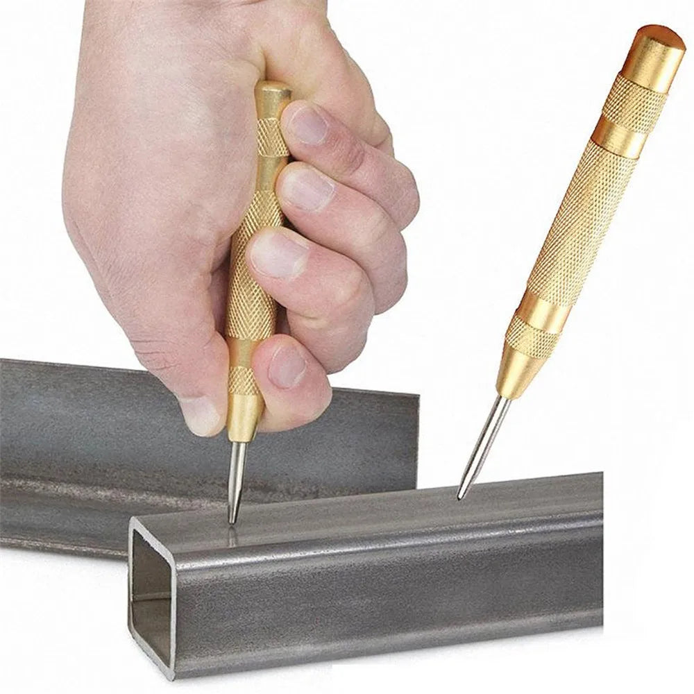 A hand holds a spring-loaded automatic center punch tool, inserting the sharp point into a metal bar.