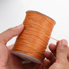 A hand is holding a spool of orange waxed cotton cord for jewelry making.
