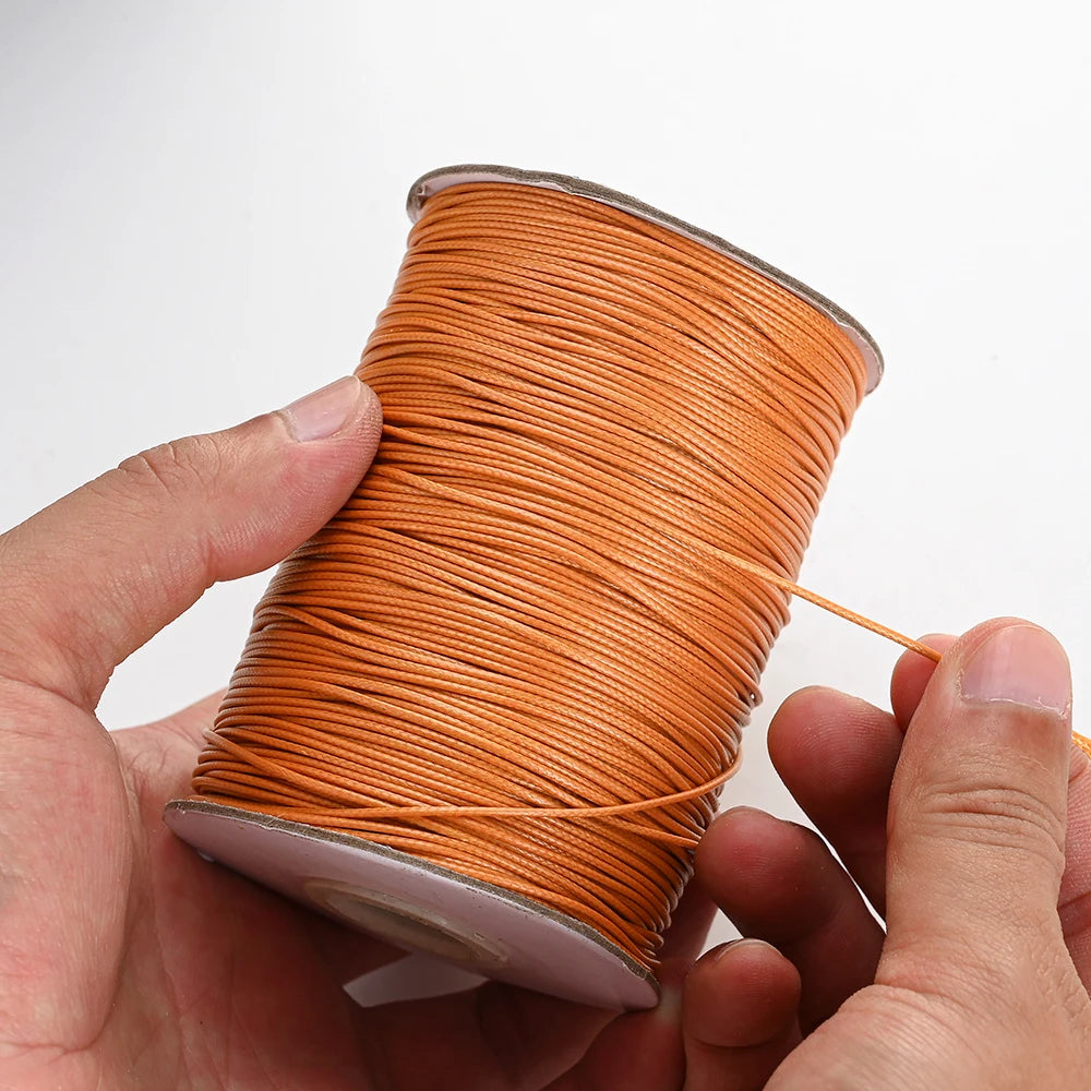 A hand is holding a spool of orange waxed cotton cord for jewelry making.