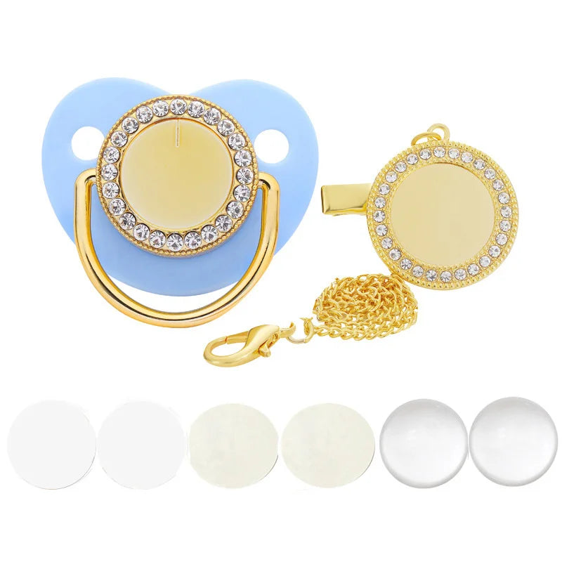 A sparkling rhinestone pacifier with a clip and a gold chain is shown against a white background.