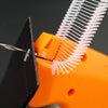 Close-up of an orange handheld tagging gun with a metal barb being inserted into a black material.