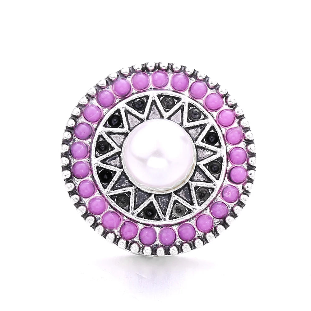 A circular silver metal snap button featuring a central white pearl surrounded by purple and black faceted stones.