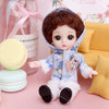 A cute baby fashion doll with brown hair wearing a blue outfit and pink accents sitting next to some macarons.