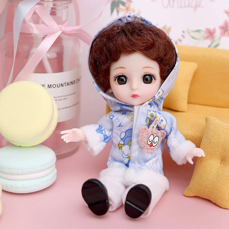 A cute baby fashion doll with brown hair wearing a blue outfit and pink accents sitting next to some macarons.