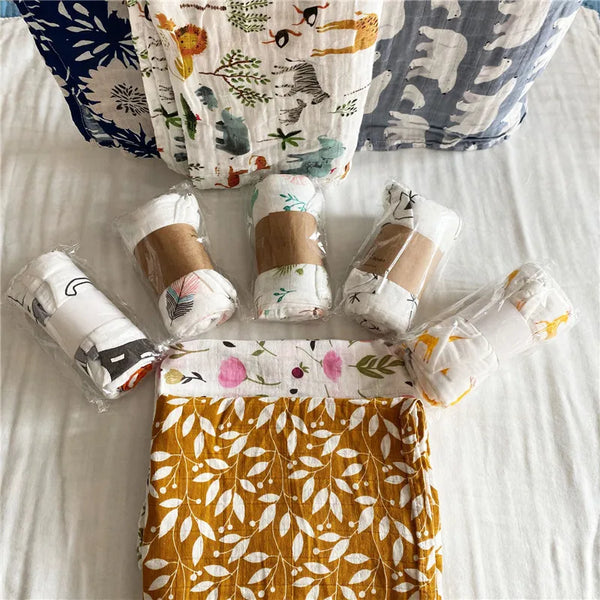 A stack of white and floral patterned muslin swaddles and a yellow leaf pattern fabric are displayed on a white bed.
