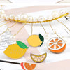 A gold beaded wreath featuring enamel fruit pins, including a lemon and an orange slice.