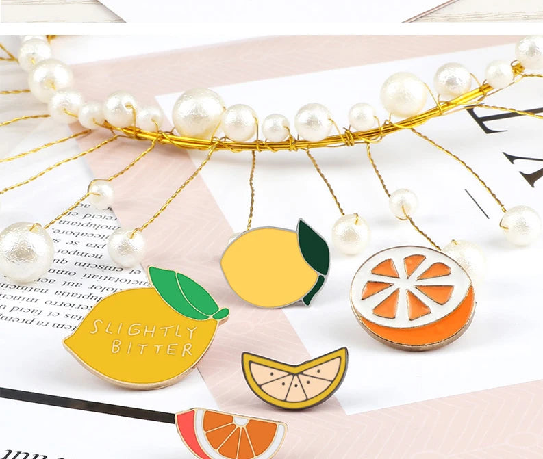 A gold beaded wreath featuring enamel fruit pins, including a lemon and an orange slice.