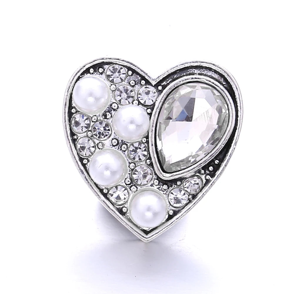 A heart-shaped silver metal snap button featuring clear and white pearls and rhinestones for jewelry making.