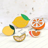 A yellow lemon enamel fruit brooch pin with a green leaf, set against a white background.