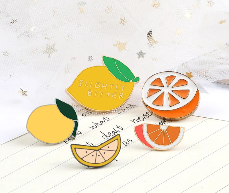 A yellow lemon enamel fruit brooch pin with a green leaf, set against a white background.